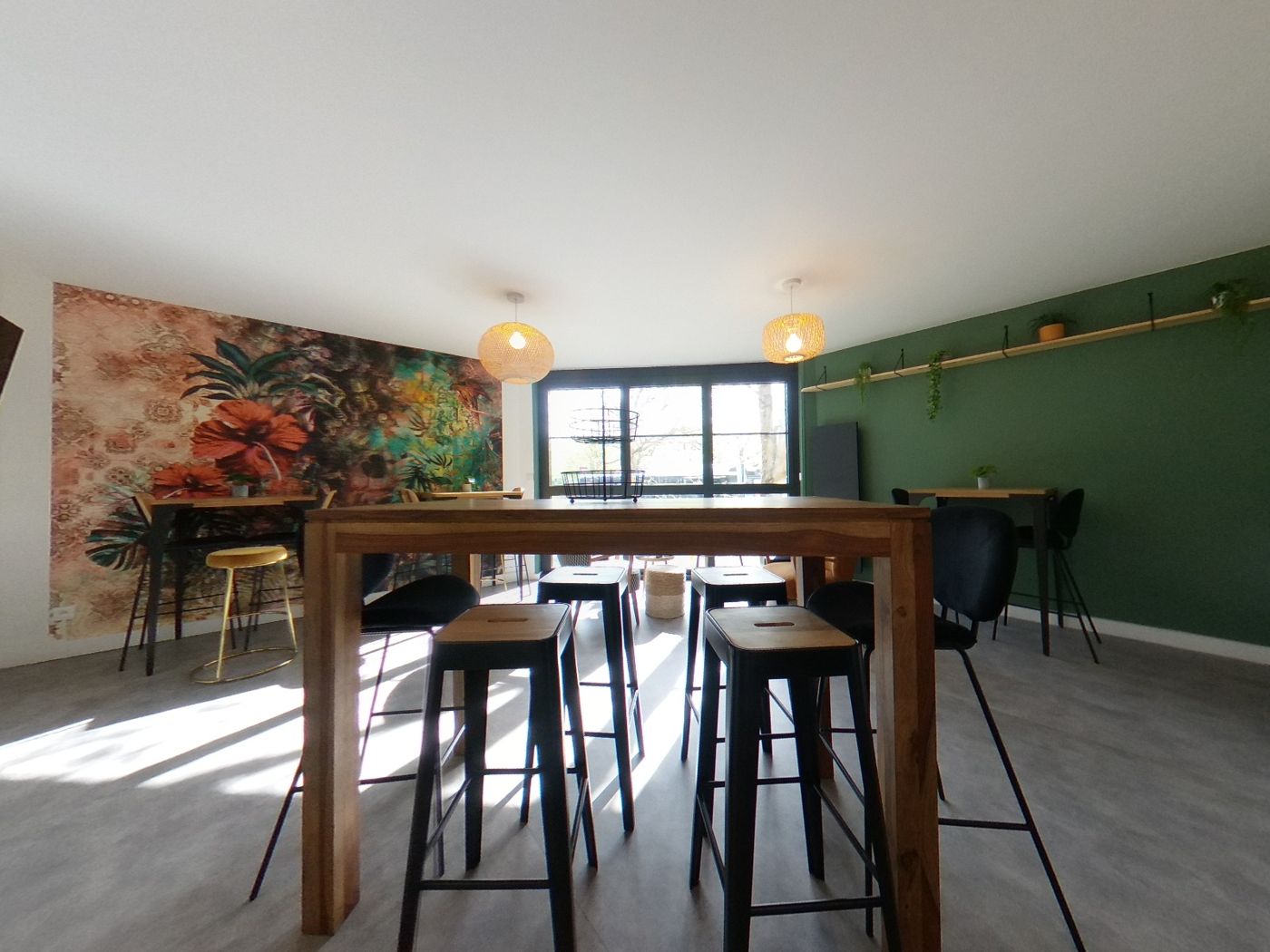 Cafétéria avec grande table haute en bois et papier peint fleuri.